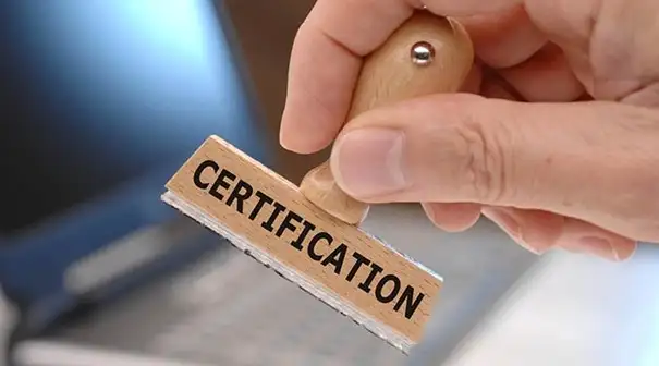 Рука тримає дерев’яний штамп із написом "CERTIFICATION" — позначення проходження сертифікації.