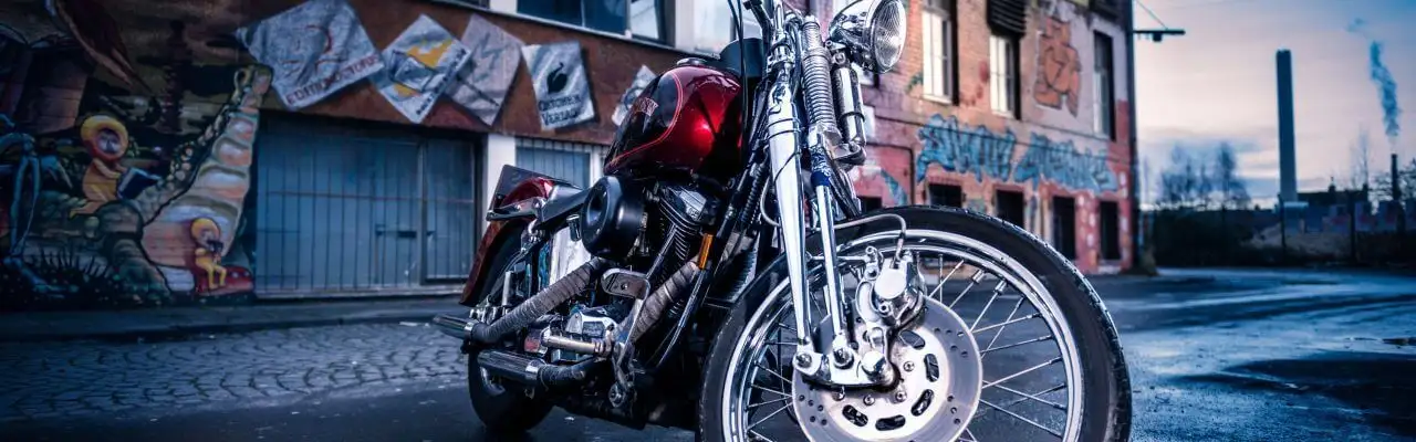 Червоний мотоцикл Harley-Davidson з хромованими елементами припаркований на мокрій бруківці біля будівлі з графіті