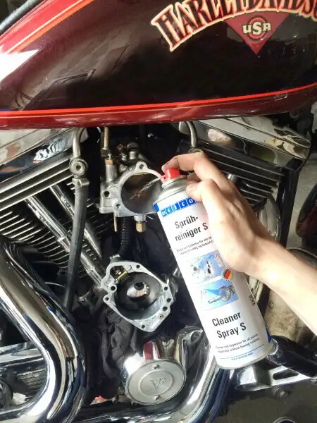 Людина розпилює очищувач Weicon Cleaner Spray S на розібраний карбюратор мотоцикла Harley-Davidson з хромованим двигуном