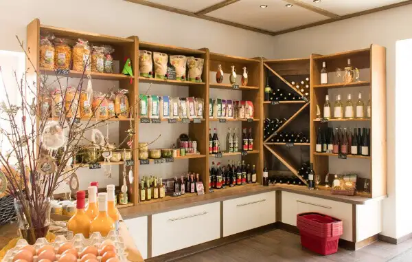 Полки с разнообразными продуктами: макароны, напитки, яйца, соусы и вино, аккуратно расставленные в светлом фермерском магазине.