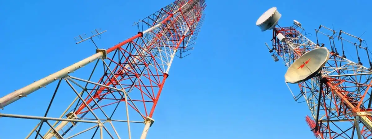 Зображення високих металевих радіовеж з антенами та передавачами на фоні синього неба.