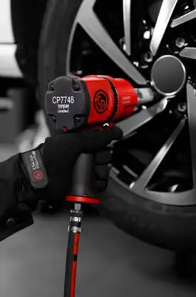 Механик в перчатках использует пневматический гайковёрт Chicago Pneumatic для откручивания болтов на колесе автомобиля.