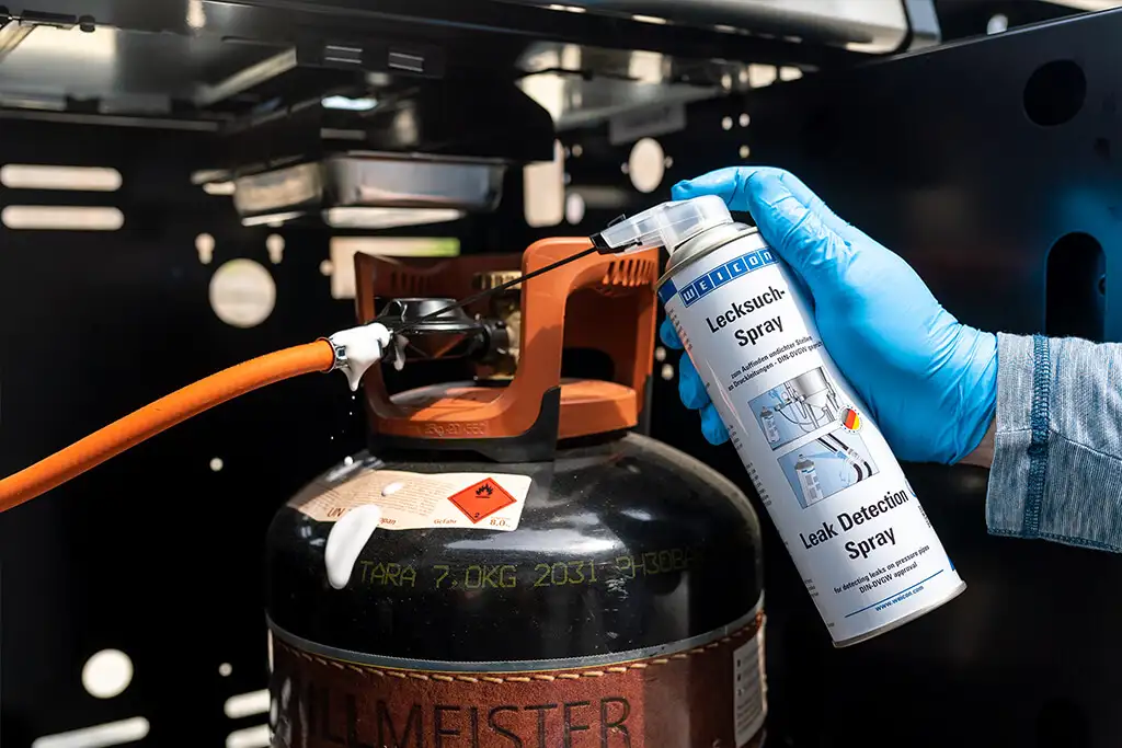 Використання спрею Weicon Lecksuch-Spray (Leak Detection Spray) для перевірки герметичності з'єднання газового балона з редуктором та шлангом газового гриля, з видимими бульбашками на місці витоку.