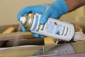 Рука в синій рукавичці тримає аерозольний балончик Surface Cleaner для знежирення та очищення поверхні