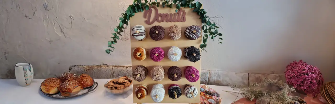 Декоративний стенд або стіна для пончиків (Donuts), прикрашений зеленню, з різнокольоровими пончиками, розміщений на святковому столі.