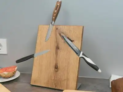 **Готовий магнітний блок для ножів DIY** із натурального дерева, встановлений на кухонній стільниці на опорній підставці; до нього примагнічено три різні кухонні ножі.