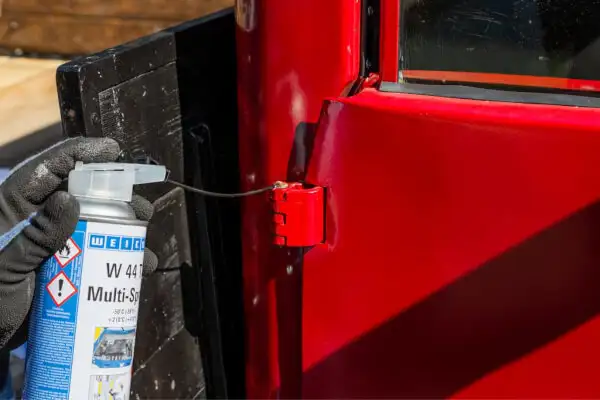 Застосування спрею W 44 T Multi-Spray для змащування дверних шарнірів червоного олдтаймера, що забезпечує догляд та обслуговування.