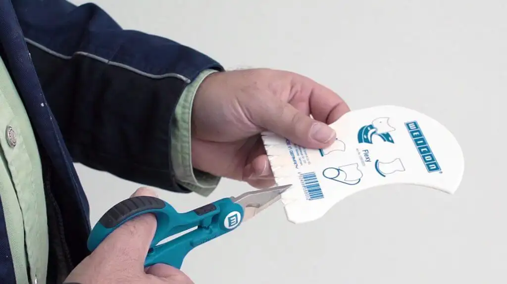 Людина відрізає частину пластикового шпателя Weicon Contour Spatula Flexy, щоб створити зубці для рівномірного нанесення та розподілу клею.