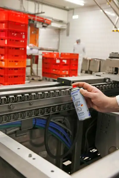 Працівник наносить технічний спрей WEICON (з допуском NSF-A1, наприклад, пінний або швидкий очищувач) на обладнання конвеєра харчової промисловості (виробництво напоїв). Використання хімії з допуском для безпеки продукції.