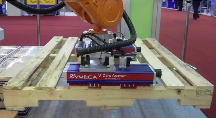 Вакуумний захоплювач VMVMECA V-Grip System, встановлений на роботизованій руці, демонструє захоплення та переміщення дерев'яного піддону (палети) на промисловій виставці.