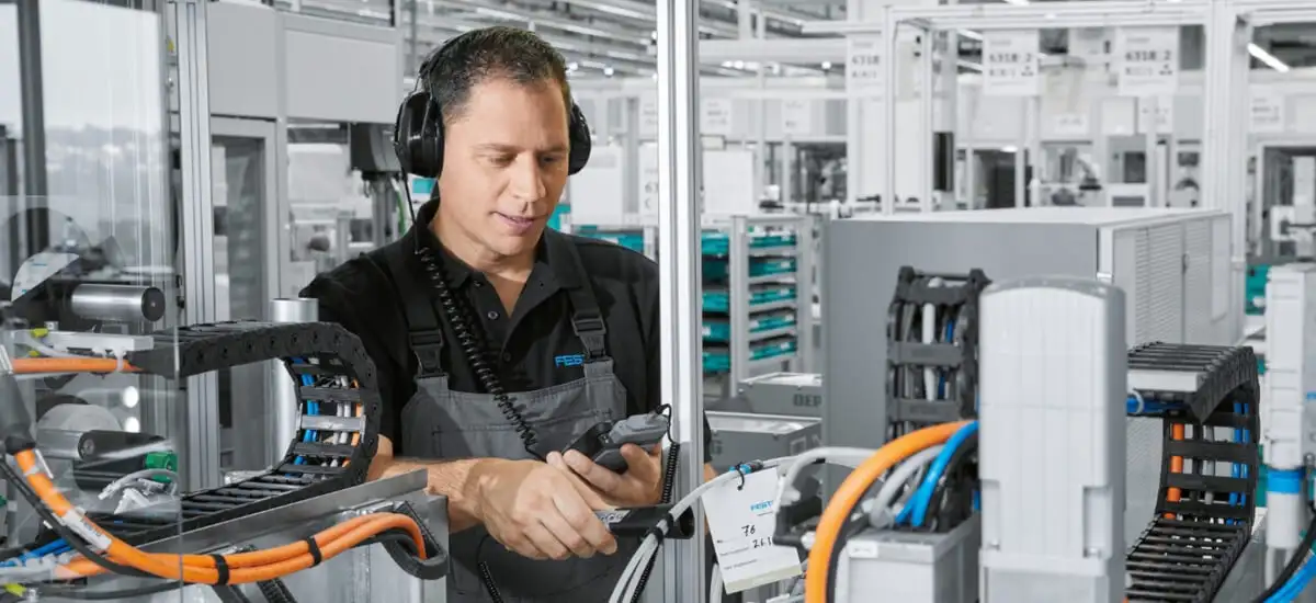 Працівник у навушниках на виробничій лінії Festo, що займається налагодженням обладнання, яке використовує принципи механіки та закону Гука.